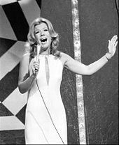 A woman, wearing a dress, holding a microphone.