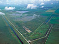 A color photograph taken from the air showing orderly sugarcane fields bordered by canals; to the south are the Everglades in a more natural state; in the center are a series of manmade cement ponds that act as stormwater treatment areas