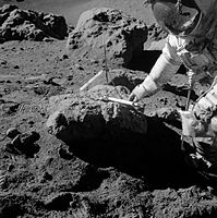 A man in a spacesuit leans over a large rock