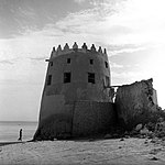 منظر لأحد أبراج قلعة دارين مع واجهة قصر الفيحاني المُطلّة على البحر