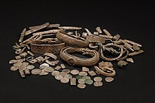 Photo sur fond noir d'un tas d'objets en argent comprenant de gros bracelets, des morceaux de métal et des pièces de monnaie