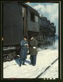 Atchison, Topeka, and Santa Fe railroad conductor George E. Burton and engineer J.W. Edwards comparing time before pulling out of Corwith railroad yard for Chillicothe, Illinois; Chicago. March 1943.