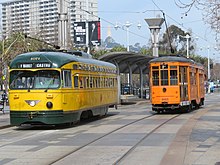 A yellow-and-green streetcar and an orange streetcar on a paved trackway