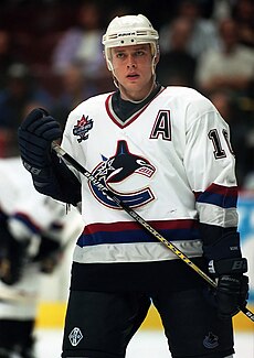 A hockey player on the ice before spectators. He wears a white jersey with a big "C", and his youthful face has a serious expression.
