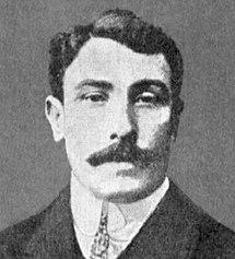 31-year-old man with a moustache. He is wearing a suit and tie