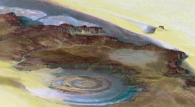 The Richat Structure is a depression in the country of Mauritania, almost 50 km (30 mi) across. It was originally thought to be the impact of a meteorite. Now it is thought to be a symmetrical uplift (circular anticline or dome) that has been exposed to erosion. In this false-color photo, bedrock is brown, sand is yellow and white, vegetation is green, and salty sediments are blue. (Credit: Landsat 7.)