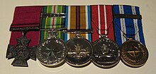 A row of five medals with the Victoria Cross on the left; the other four medals are circular with multicoloured ribbons.