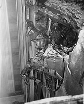 A black-and-white photo of airplane wreckage embedded in the facade, high up