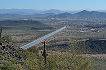 picture of a straight blue ribbon of water, the canal, running through the desert, from a vantage point of one of the mountains surrounding the city.