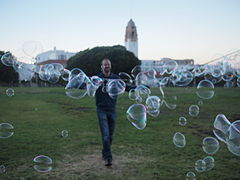 Man making large bubbles in Dolores Park. View of Mission High School in background