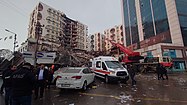 Image of a white ambulance and a white personal car standing in front of the rubble of a demolished commercial centre