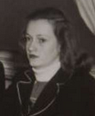 A young white woman with dark hair loose and parted on the side, wearing a dark suit jacket.