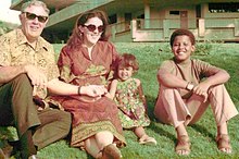 A color photograph of a couple and two children sitting in the grass.