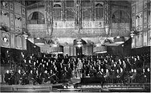 interior of a Victorian concert hall, showing the orchestra and conductor on the platform
